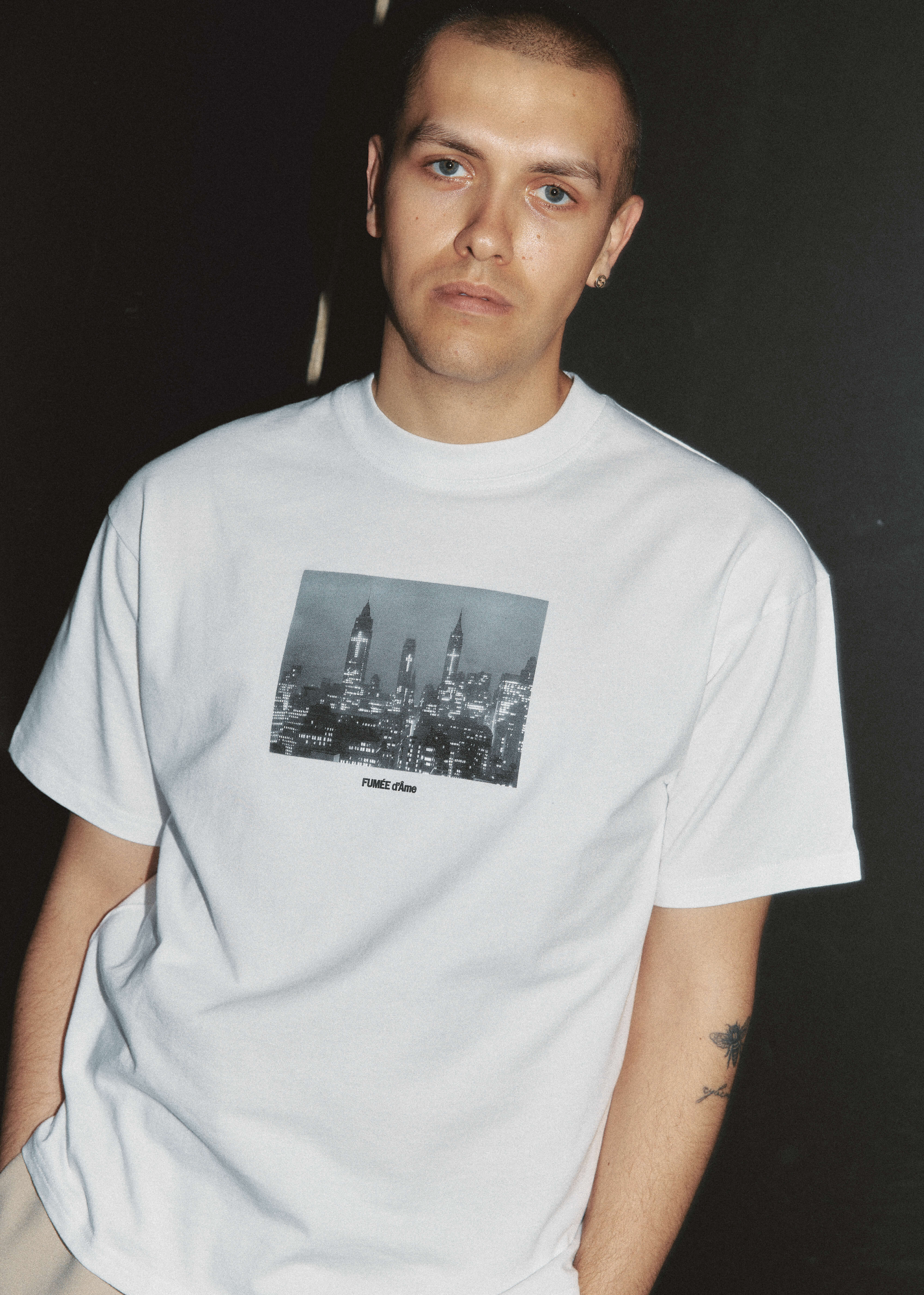 Person wearing a white t-shirt with a black and white graphic design on a dark background